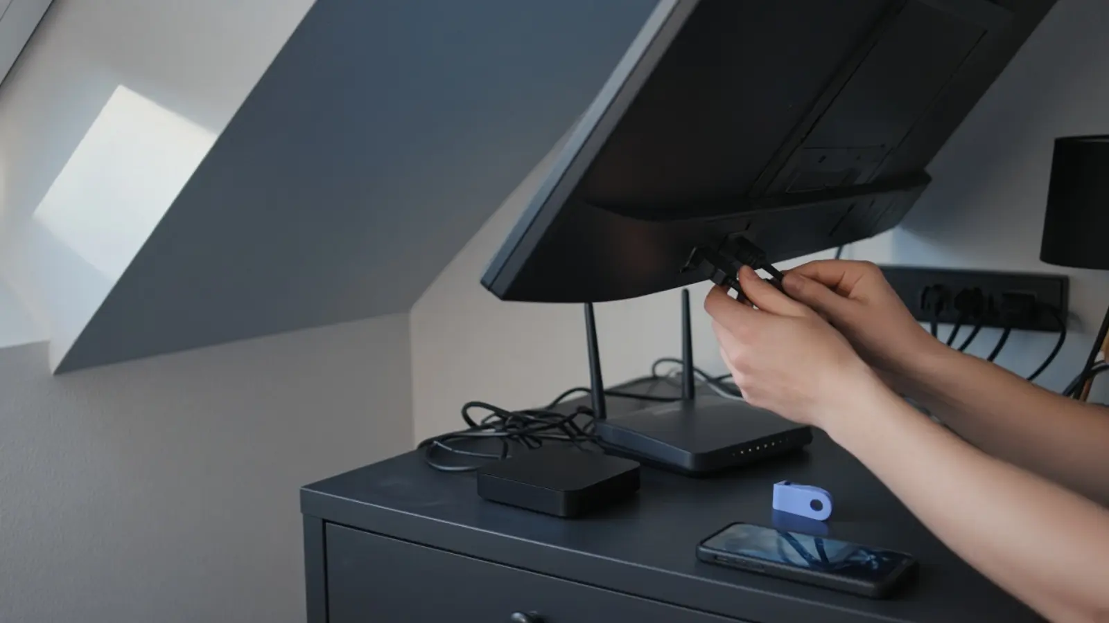 Hände stecken ein Kabel hinten in den Fernseher unter der Dachschräge